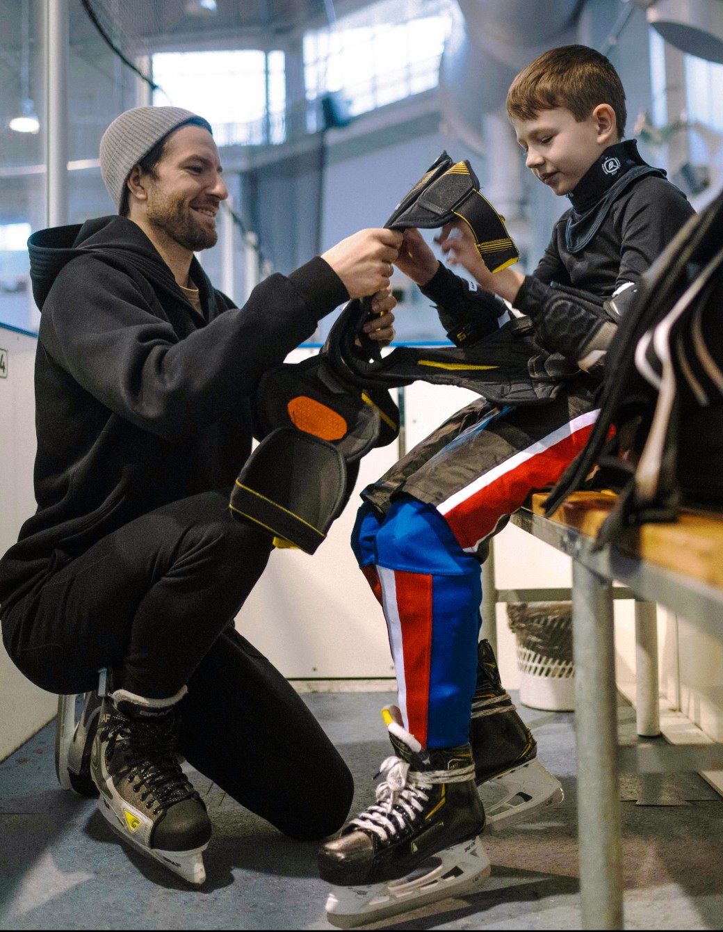 Vuxen som hjälper ett barn att ta på hockeyutrustningen i en ishall