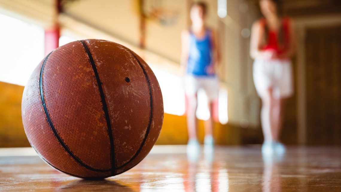 basketboll på golv i en idrottshall med två personer suddigt i bakgrunden